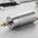 Micro DC motor and gearmotor on a workbench with engineering tools.